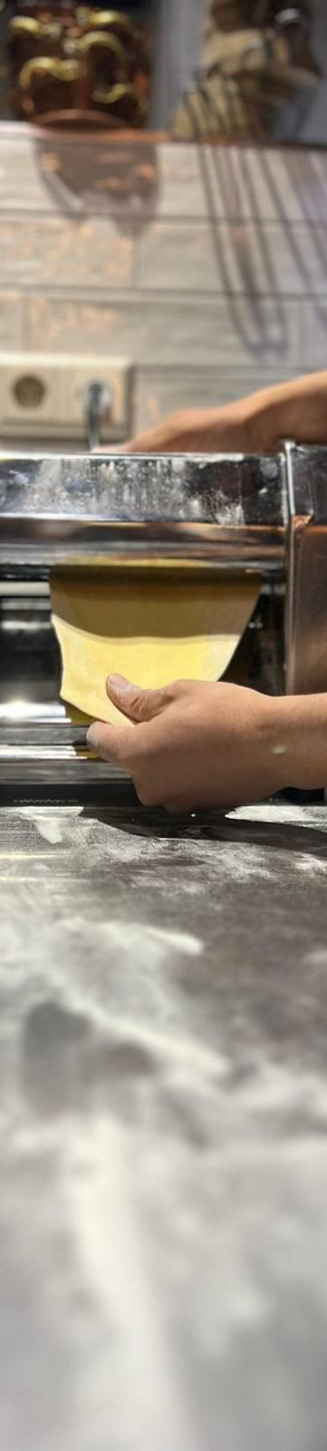 Afbeelding verse pasta Een hand rolt vers deeg uit met een pastamaker op een werkblad.